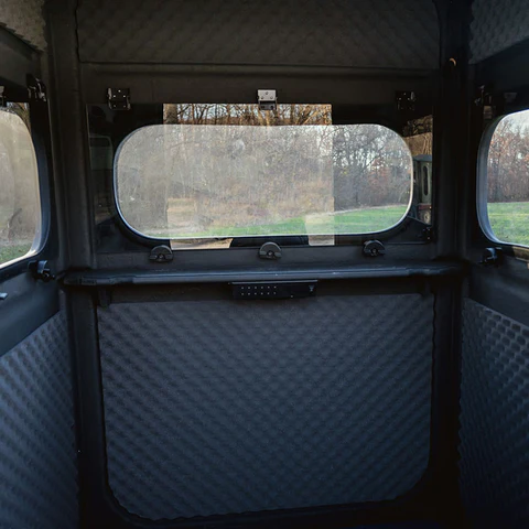 View from inside a small, foam-insulated Michigan Hunting Blind with windows, revealing a grassy landscape and trees outside—perfect for hunting in comfort. - Michigan Hunting Blinds